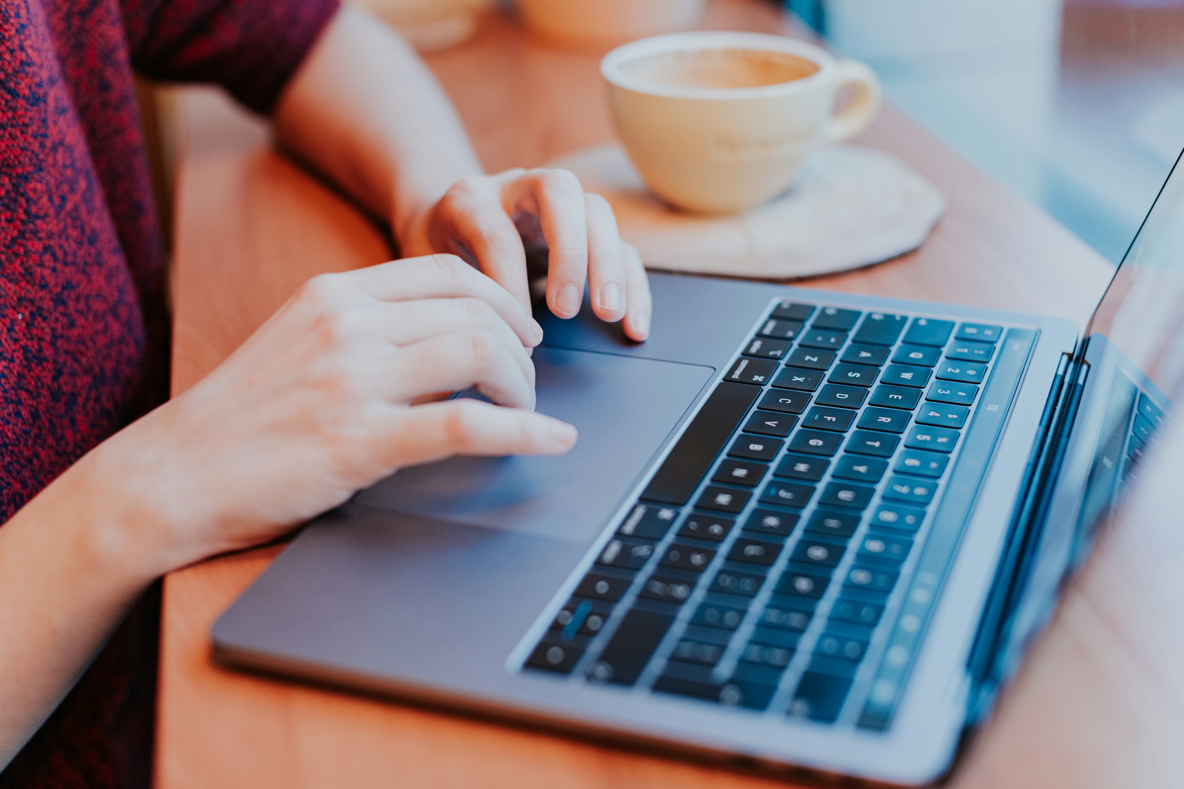 Close-up of hands typing a quick reply on a laptop at a cafe table